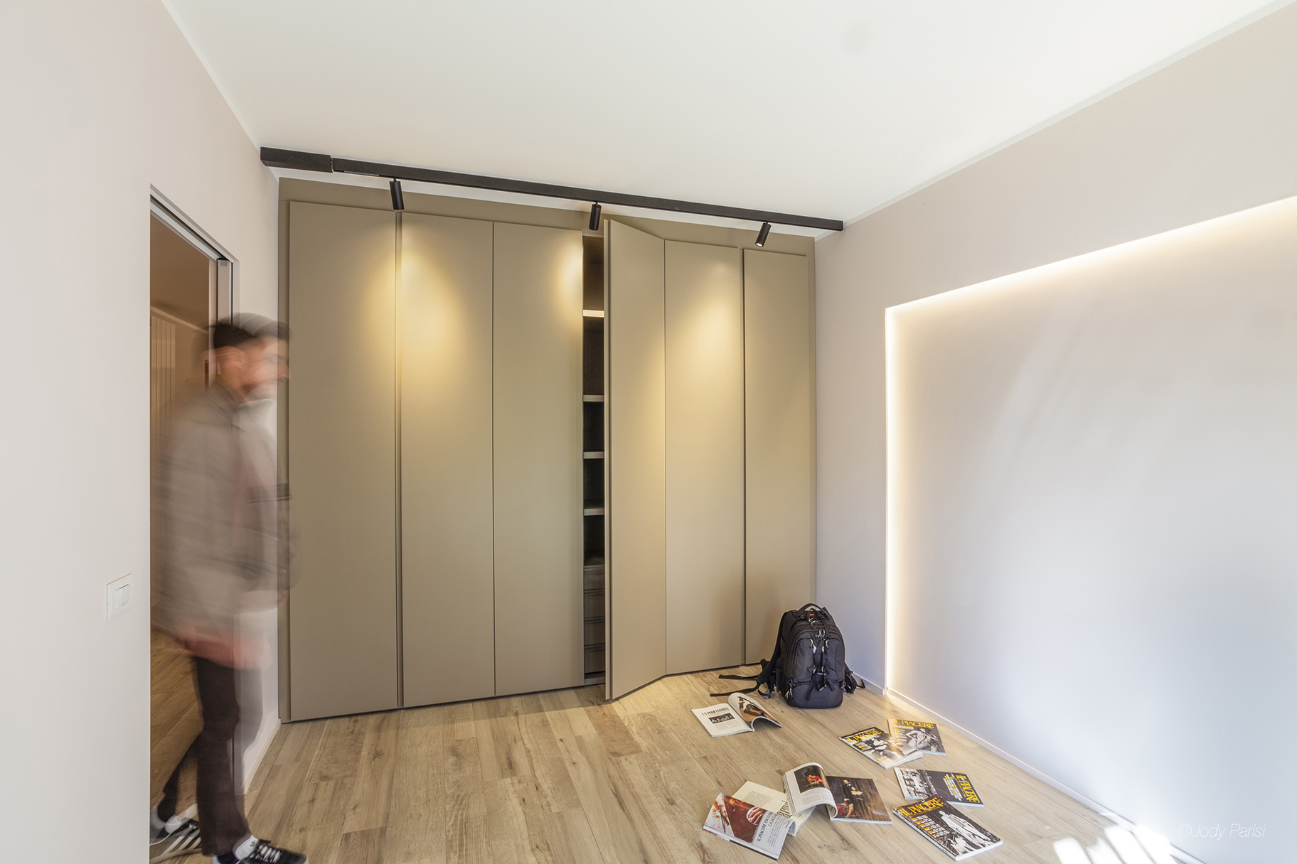 Stanza di una casa con un armadio illuminato da dei faretti da soffitto ed un uomo che guarda delle riviste per terra 