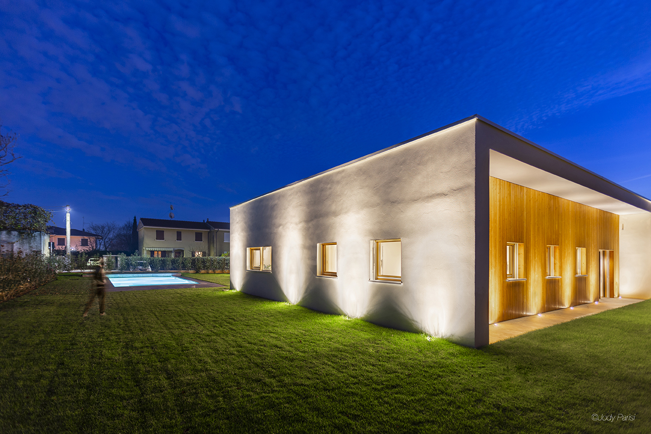Esterno di una villa moderna con giardino e piscina, illuminata da luci esterne di sera