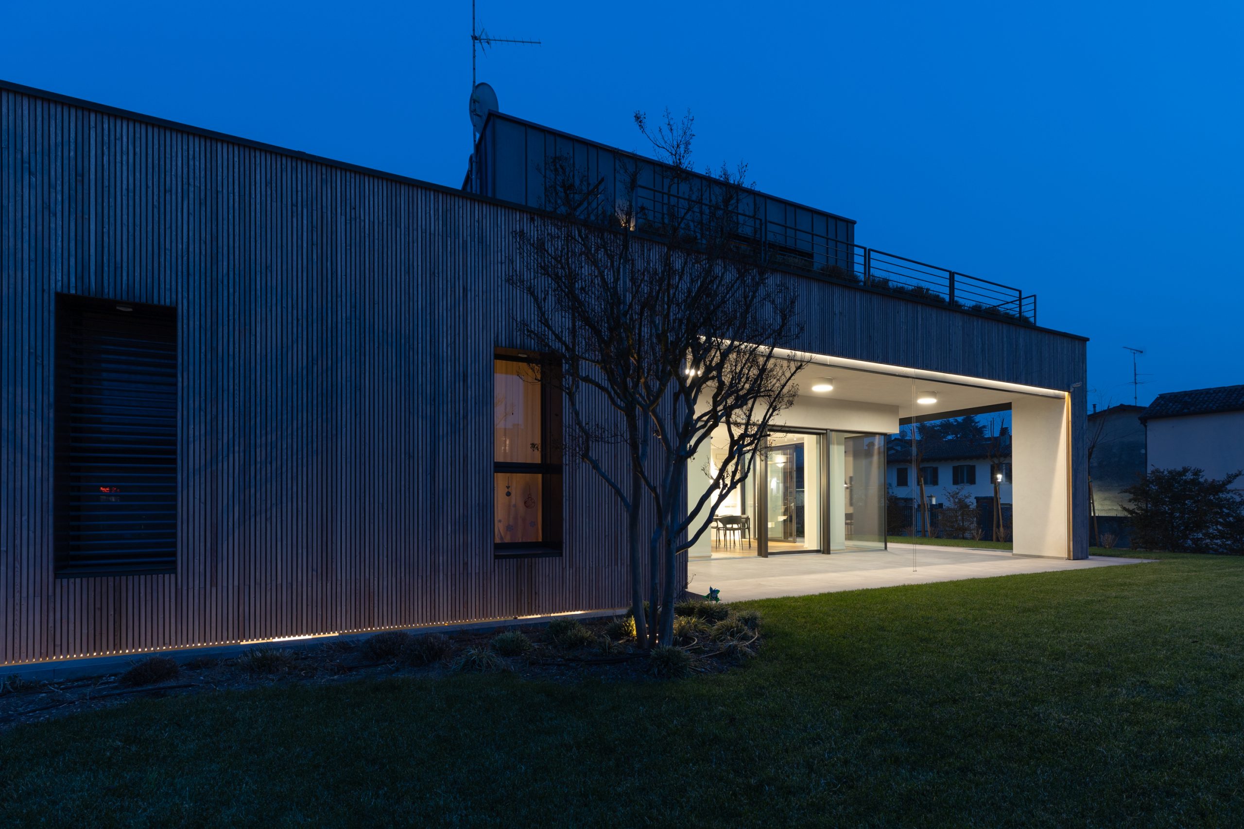 Esterno di una villa moderna con giardino, con luci da soffitto che illuminano il portico