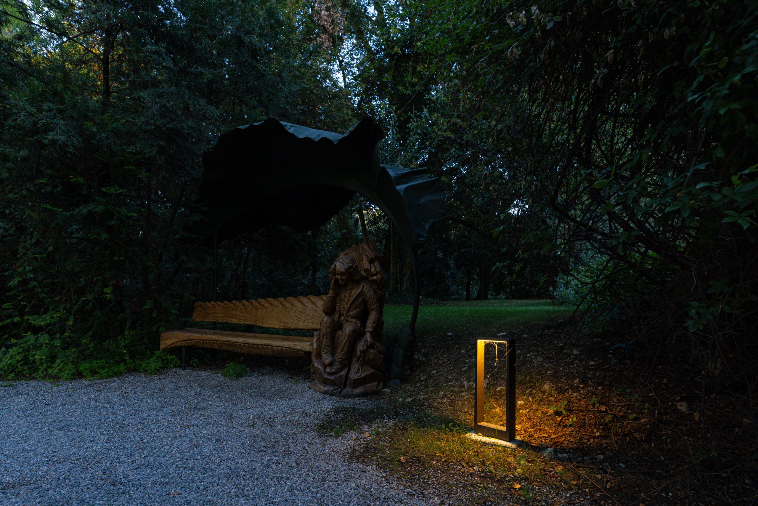 Giardino con una panchina il legno e una statua, illuminata da una luce da esterno
