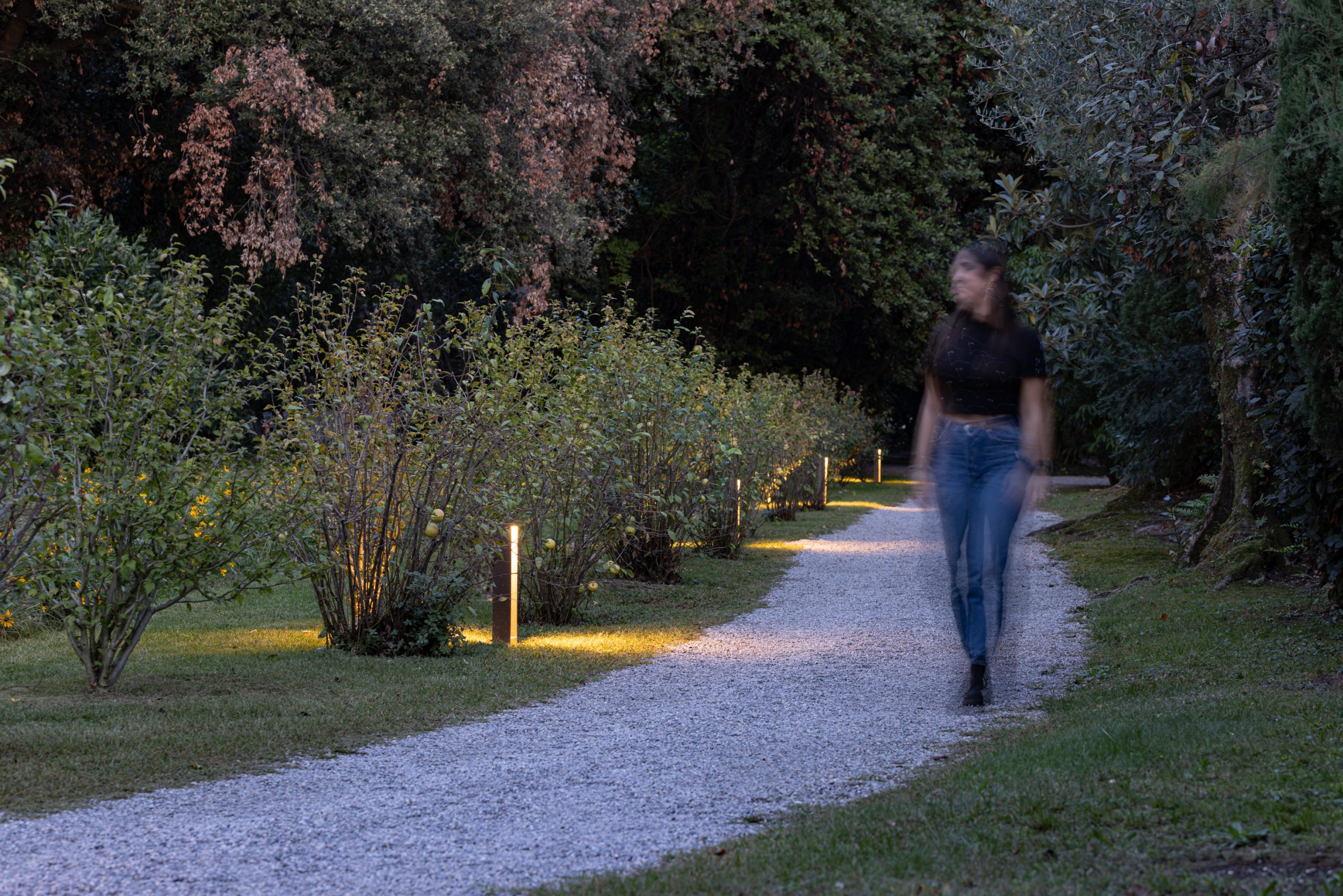 Vialetto in ghiaia di un giardino illuminato con luci da esterno e una persona che cammina