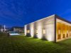 Esterno di una villa moderna con giardino e piscina, illuminata da luci esterne di sera