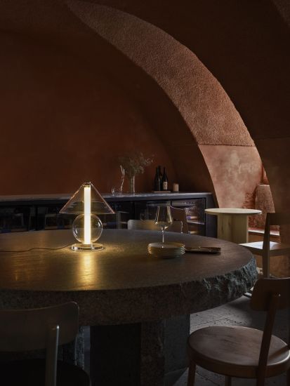 Lampada da tavolo di Marset con affianco un bicchiere da vino in una stanza buia 