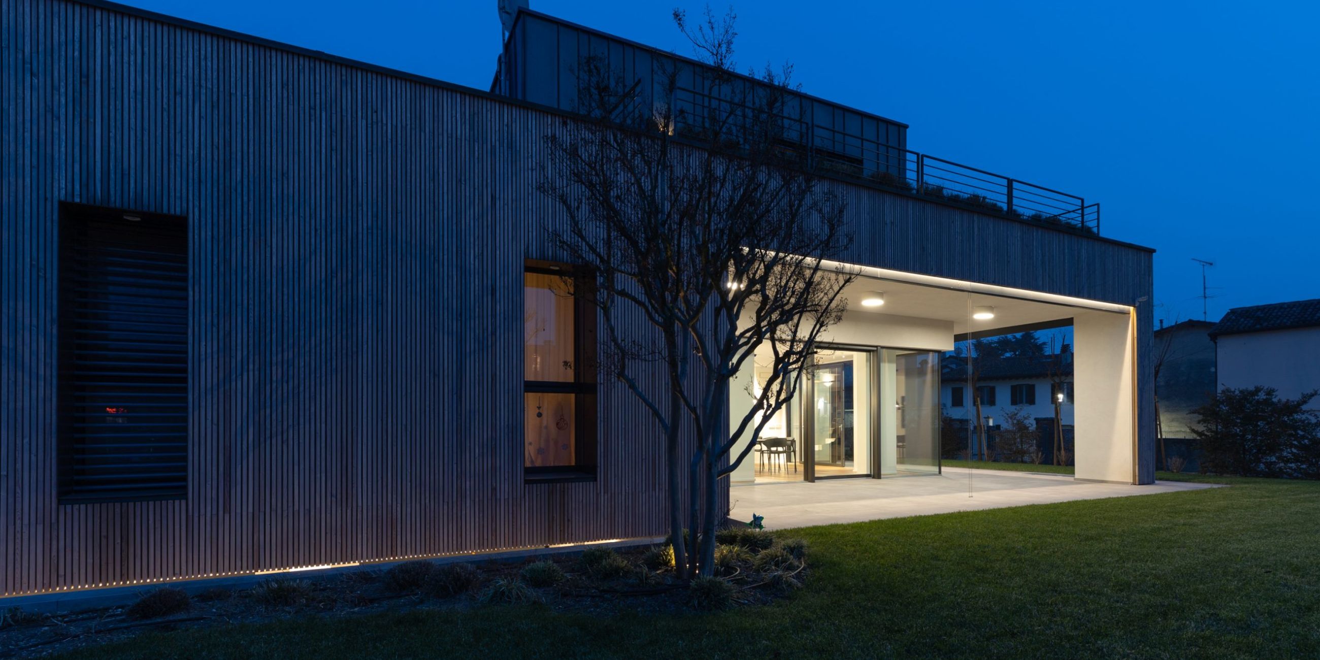 Esterno di una villa moderna con giardino, con luci da soffitto che illuminano il portico