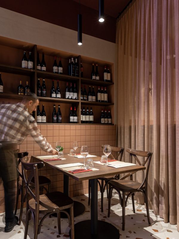 Cameriere apparecchia un tavolo in un ristorante illuminato da una luce a sospensione