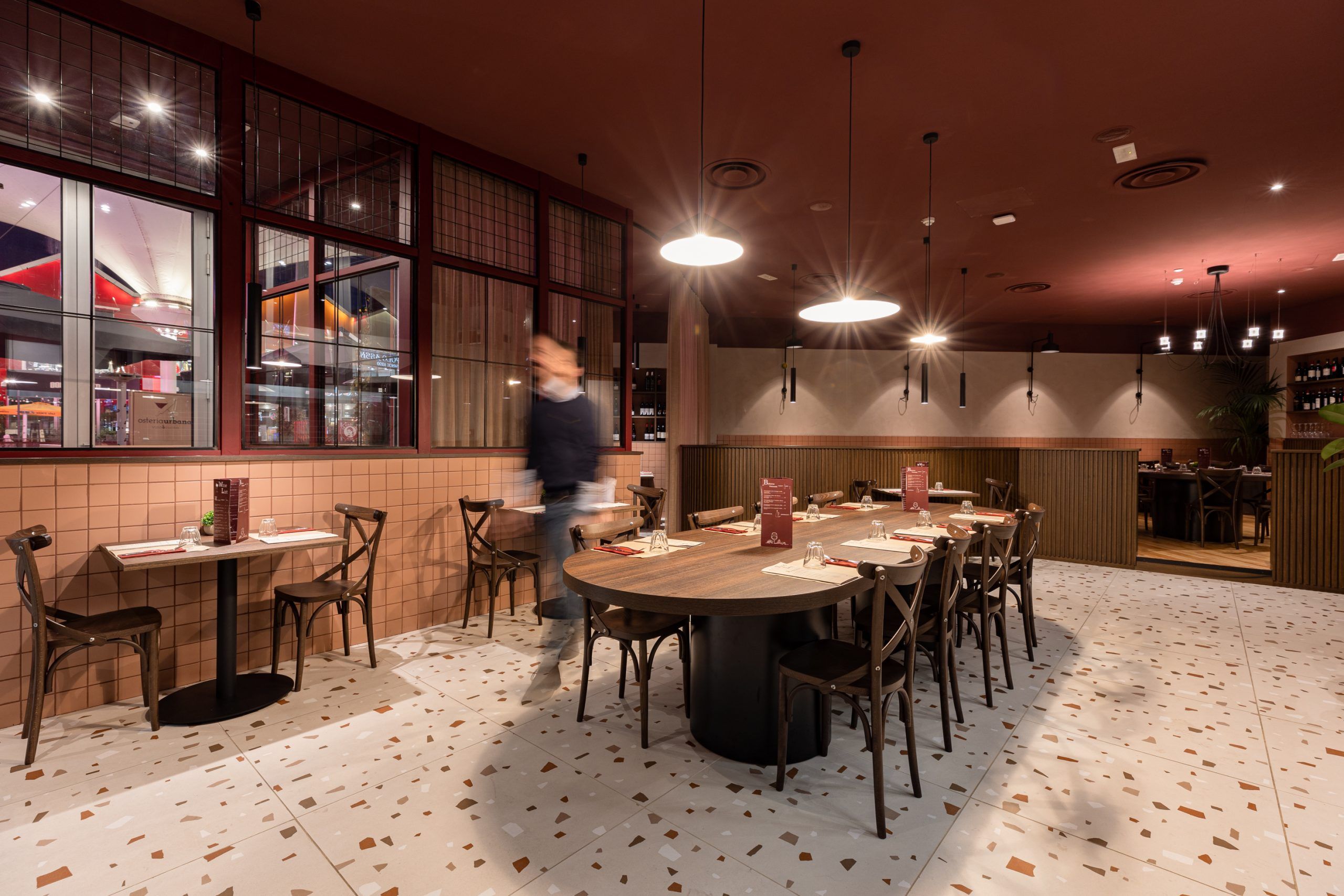 Uomo cammina in una sala di un ristorante illuminata da luci a sospensione