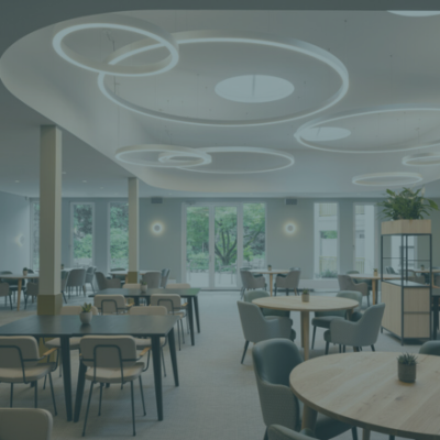 Lampade a sospensione a forma di cerchio che illuminano una sala con tavoli e sedie