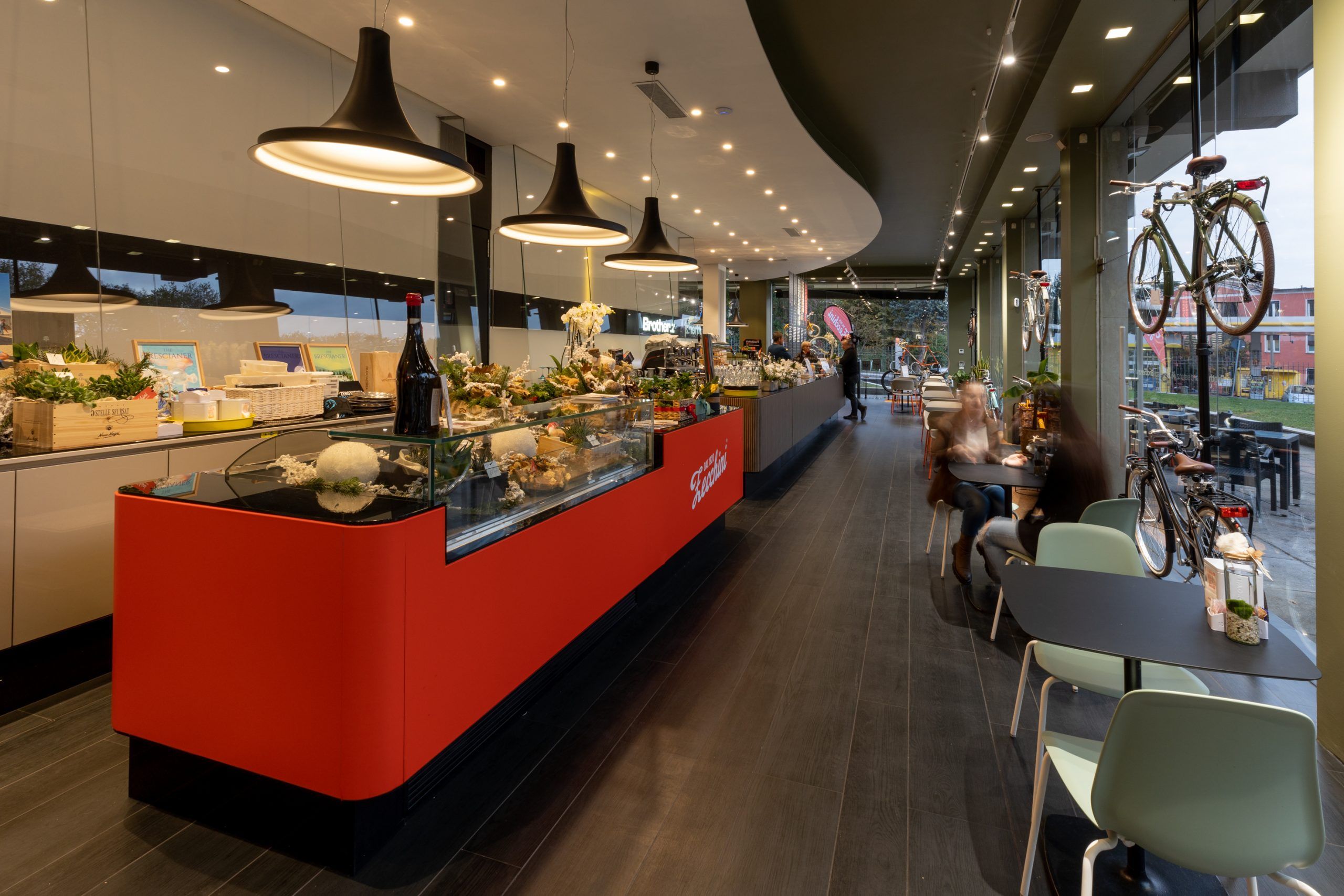 Foto in primo piano di tre lampade a sospensione di un negozio/caffetteria, in secondo piano il bancone e delle persone in piedi e sedute ai tavoli